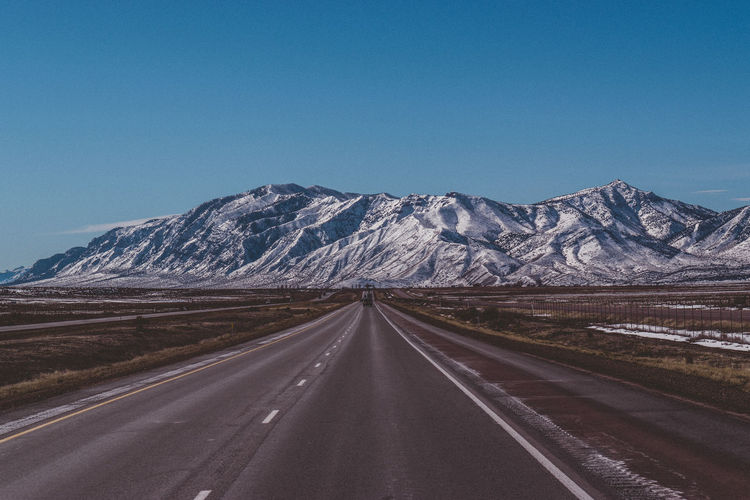 Road leading towards mountain against clear blue sky
