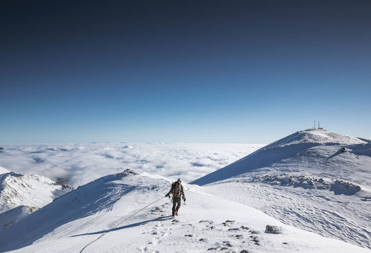 Man walking on snowcapped mountain against blue sky