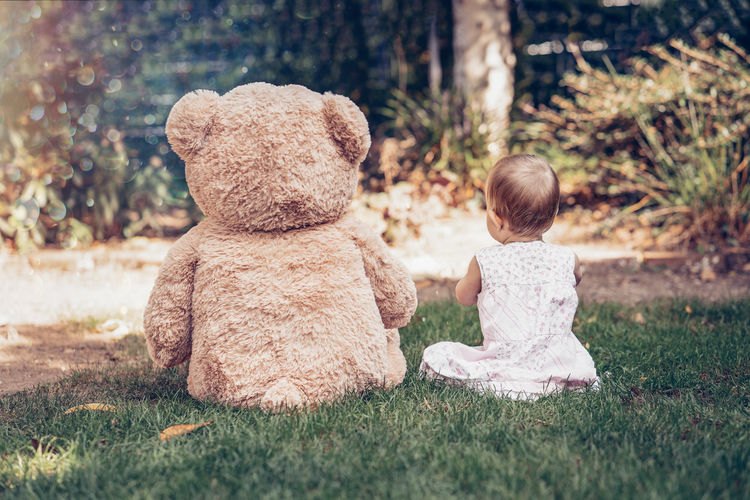 Cute little girl baby sitting with toy on gras backside summertime