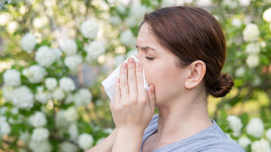 Woman blowing nose with tissue in park