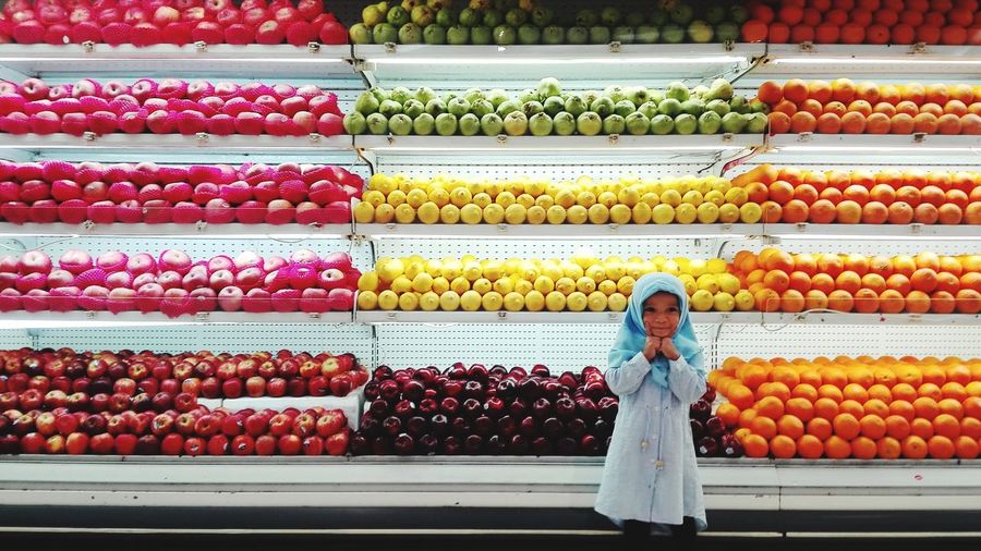 Portrait of cute girl wearing hijab standing against fruits in supermarket