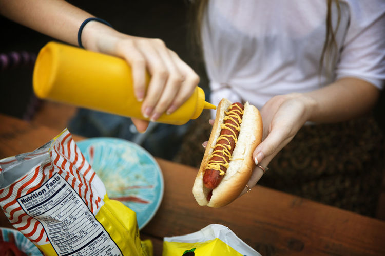 Cropped image of woman pouring mustard sauce on hot dog at garden party