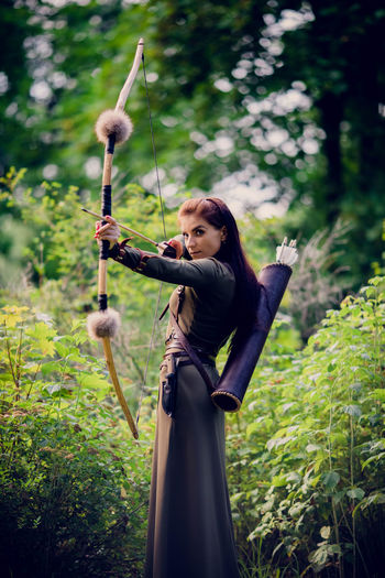 Beautiful woman holding bow and arrow standing outdoors
