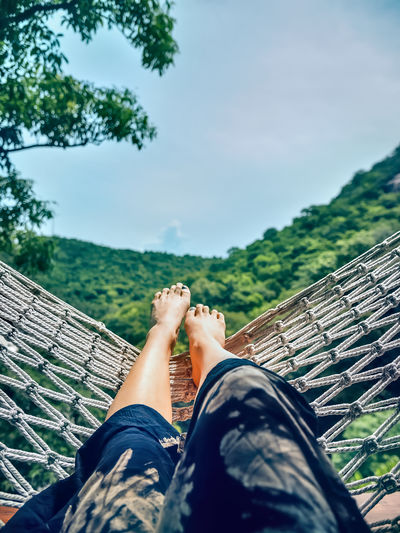 Low section of man relaxing on hammock against sky