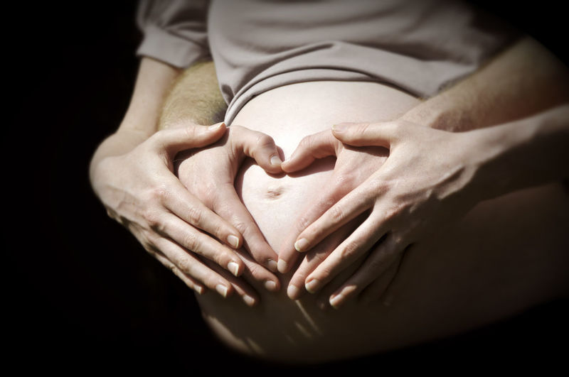 Midsection of pregnant woman holding stomach against black background