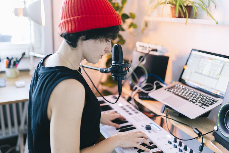 Female musician wearing knit hat while playing piano in studio