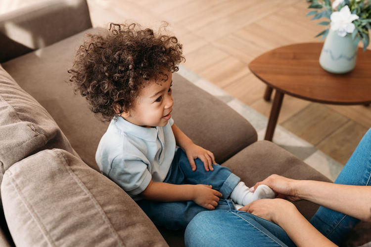 Cute boy with mother sitting on sofa at home
