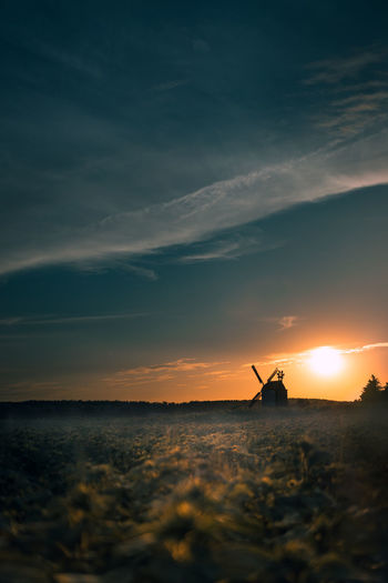 Low angle view of traditional windmill on field against sky during sunset