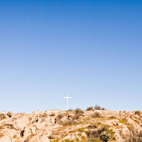 Low angle view of religious cross on rock against clear blue sky