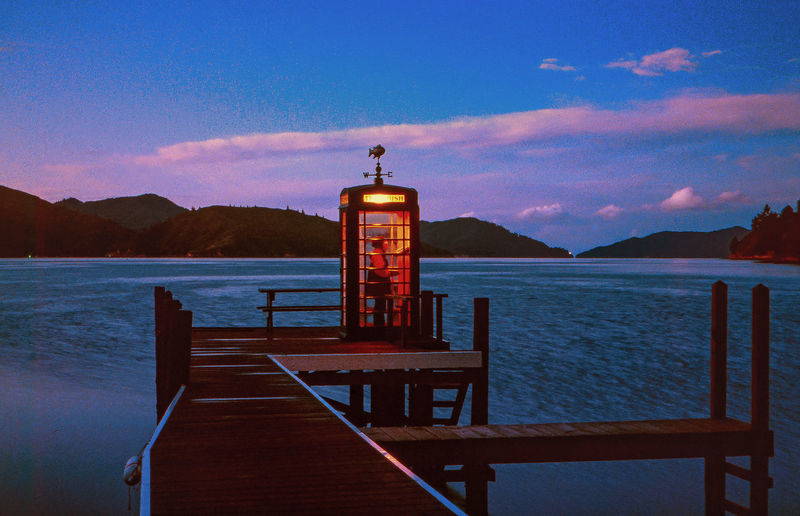 Man in telephone booth on pier by sea during sunset