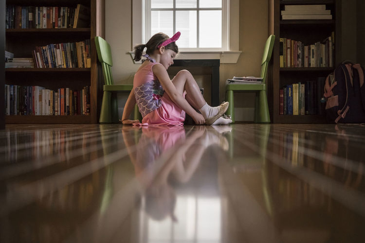 Surface level image of girl wearing shoe while sitting on hardwood floor at home