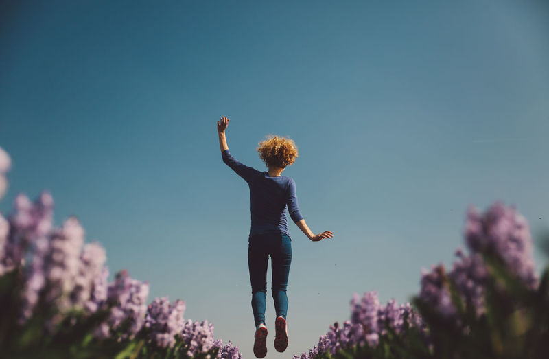Low angle view of woman jumping against clear sky