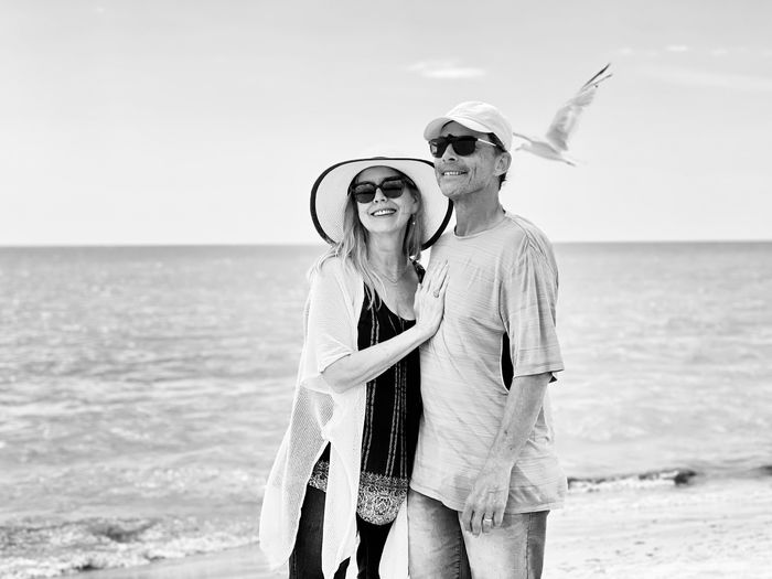 Happy senior couple  enjoying being together on beach as seagull flys by against water and sky.  