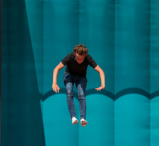 Full length of young man in mid-air against blue background