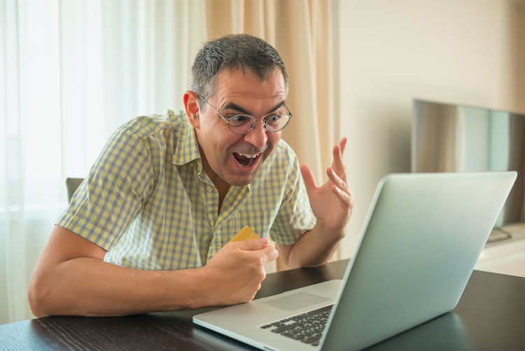 Mature man with mouth open using laptop on table while sitting at home