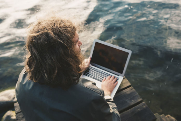 High angle view of man using laptop while sitting on jetty by lake