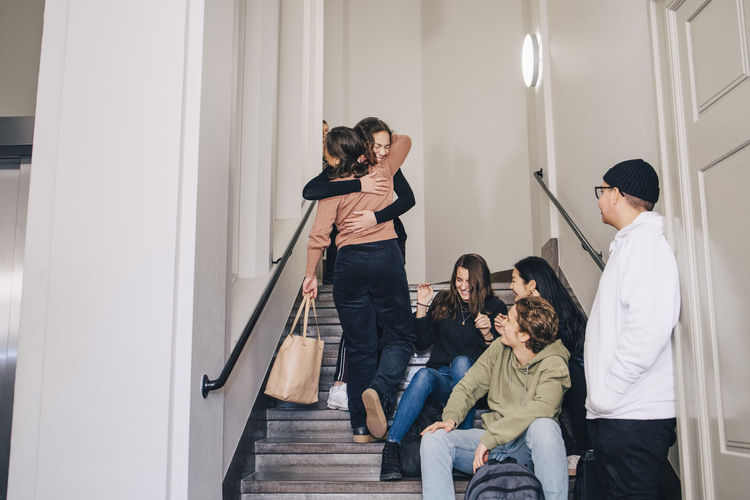 Teenagers looking female classmates embracing on steps at high school