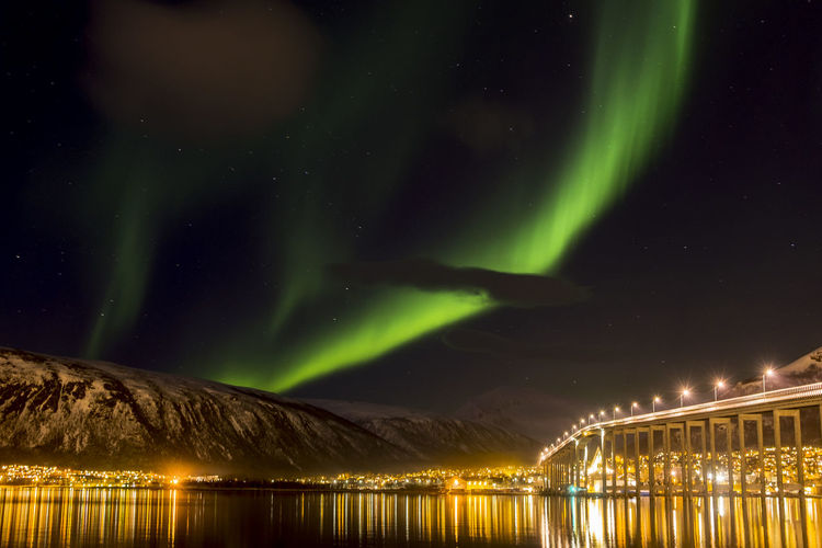 Illuminated bridge over river against aurora borealis
