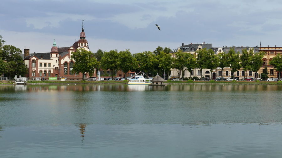 View of buildings by lake against cloudy sky