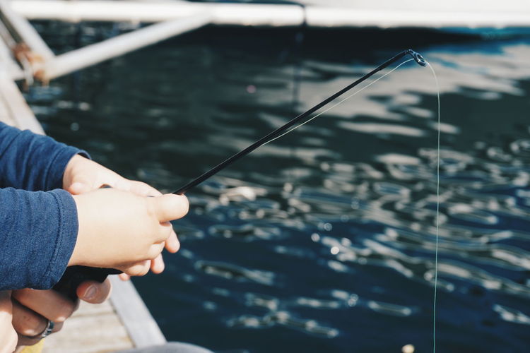 Cropped hands of parent and child holding fishing rod