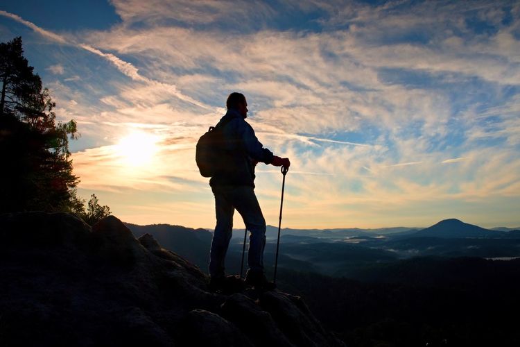 Silhouette of tourist with poles in hand. hiker with sporty backpack stand. sunny spring daybreak