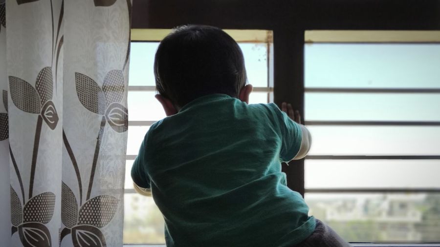 Rear view of boy looking through window at home