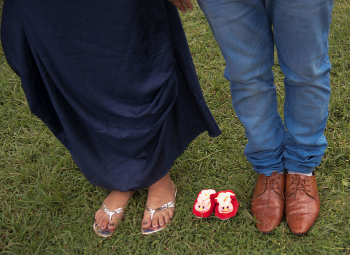Low section of couple with baby booties standing on grass