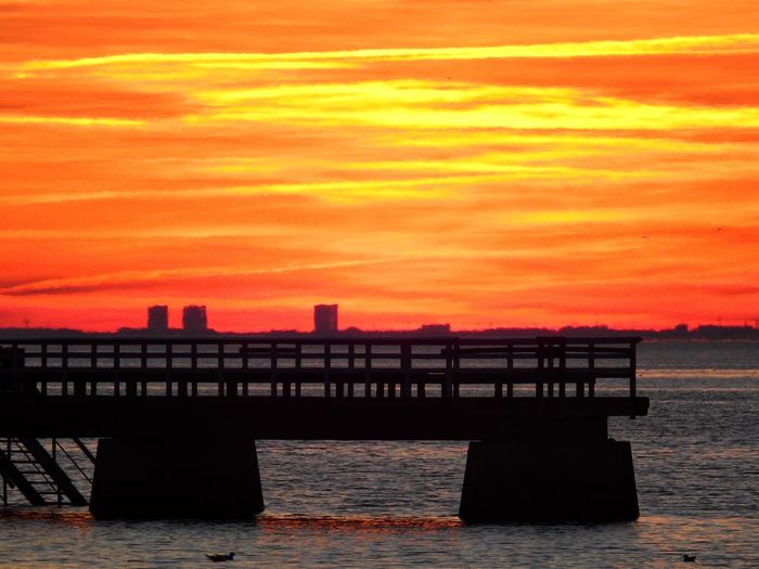 Silhouette pier over sea against orange sky