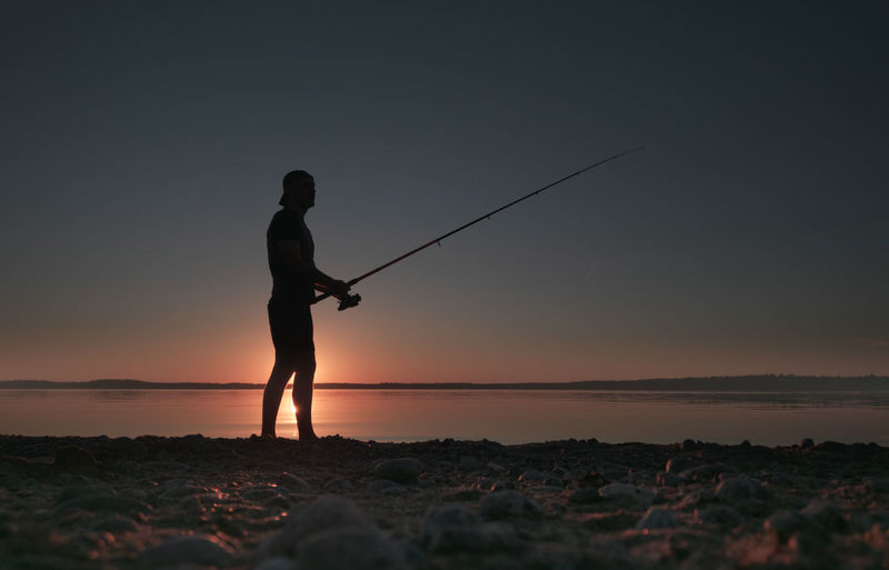 Silhouette of a fisherman with a fishing rod in his hands on the background of the low sun. 