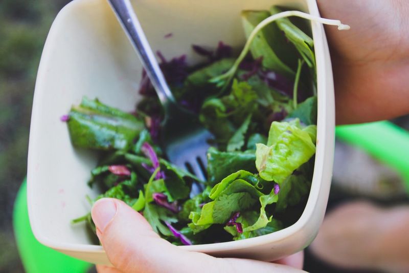 Cropped image of hands holding bowl with salad
