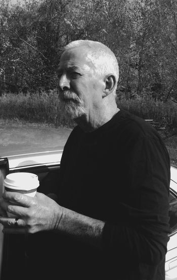 Thoughtful man holding disposable coffee cup standing near car