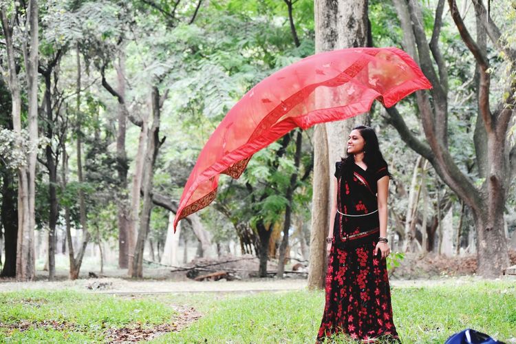 Young woman wearing traditional clothing while looking at dupatta flying in air at park