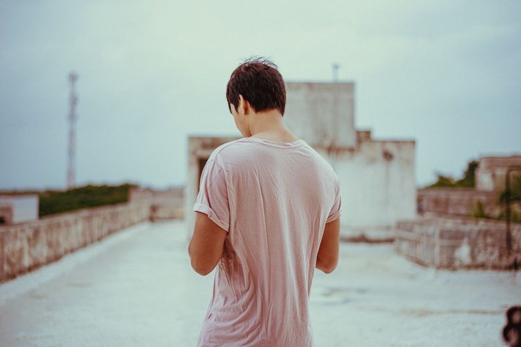 Rear view of man standing against sky in city