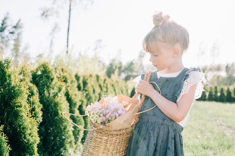 Young girl carrying beautiful flowers in a basket outside in summer