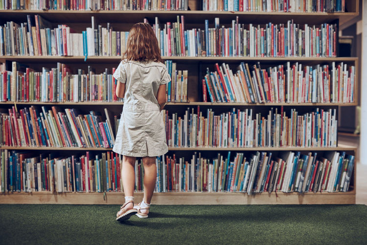 Student choosing book in school library. girl selecting literature for reading. books on shelves
