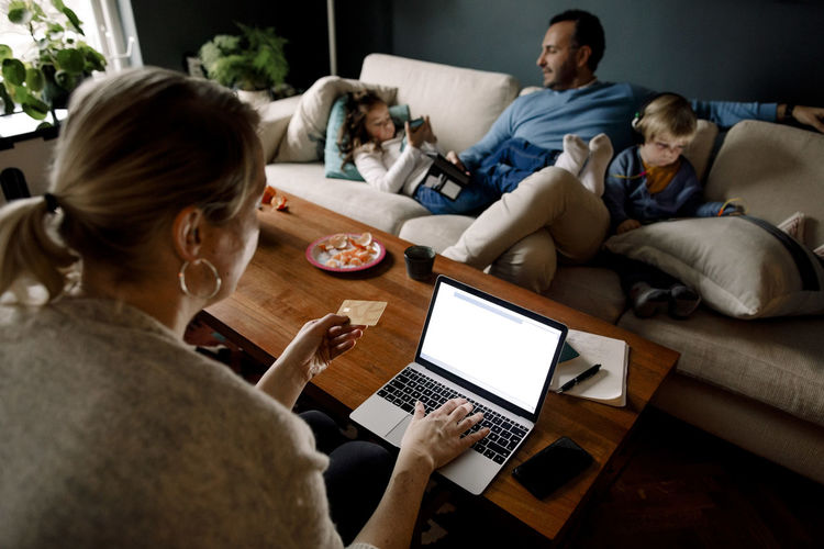 Mother online shopping while man and daughters using various technologies in living room