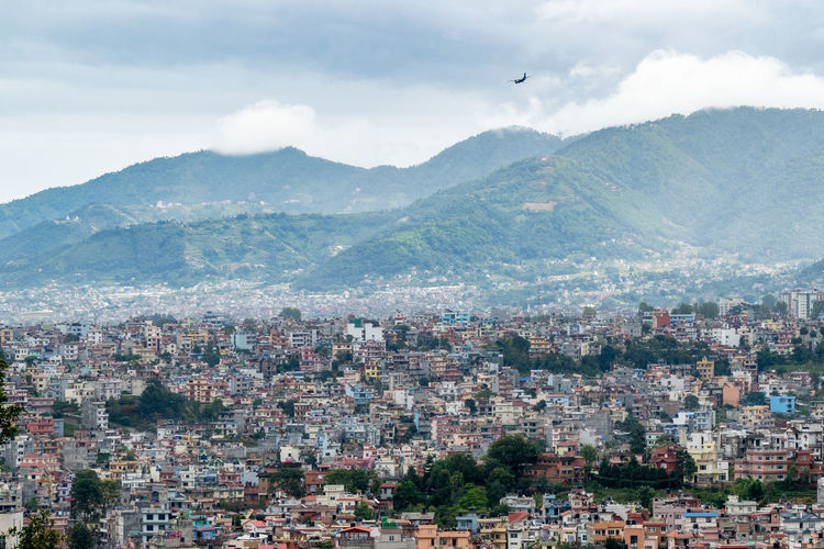 A view of the population density in city of kathmandu under a stormy sky with an airplane coming in.