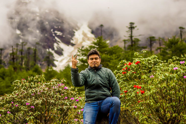 Portrait of man showing peace sign against flowering plants at garden
