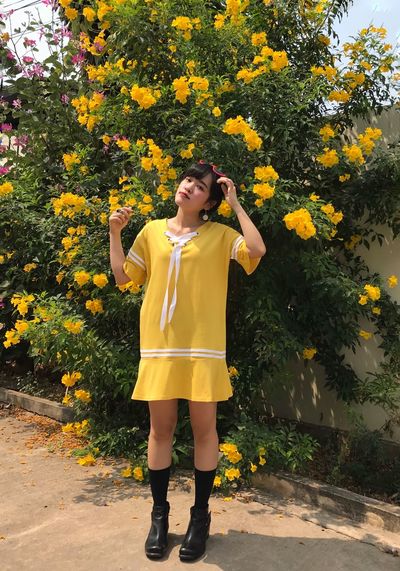 Full length of a woman standing on footpath agent yellow flowers plants 