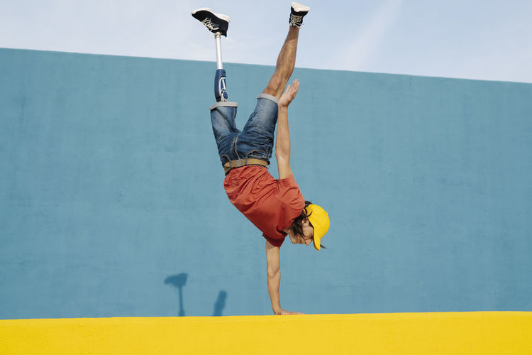 Young man with artificial limb and foot doing handstand against multi colored wall