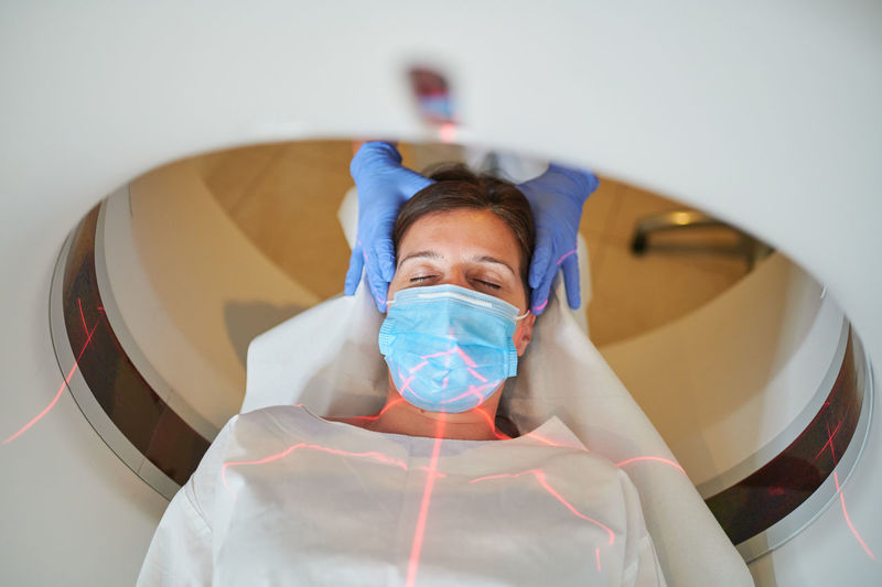 Anonymous doctor in uniform using tomography machine with lying female patient in hospital