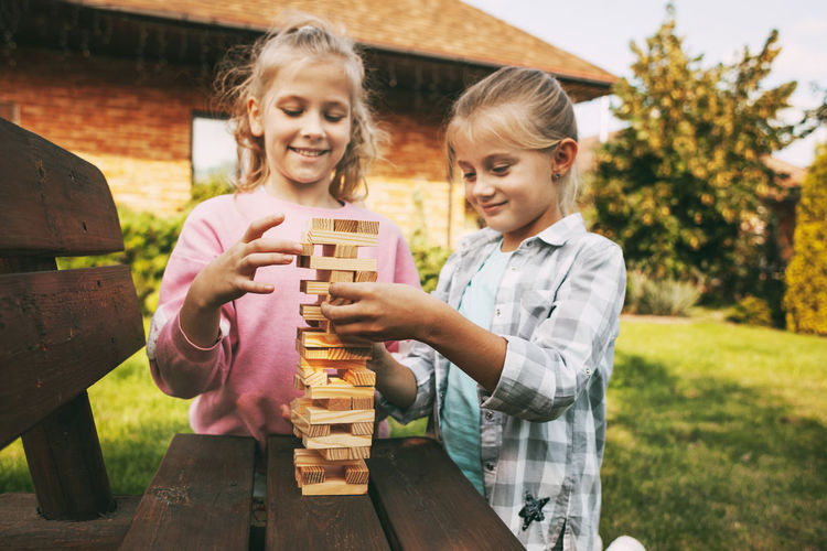 Two girls are having fun and playing a wooden board game outdoors near their home.