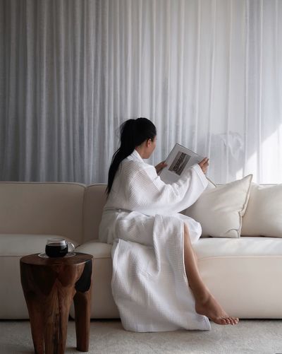 Sitting on the white sofa with a robe on and reading a book