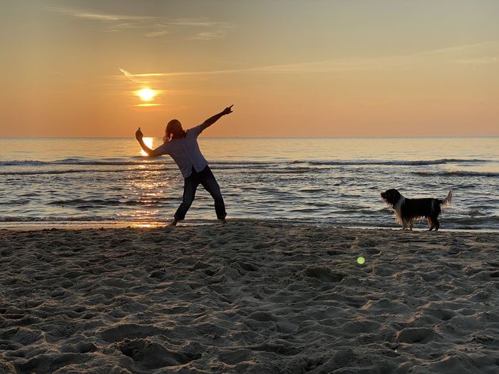 People with dog on beach against sky during sunset