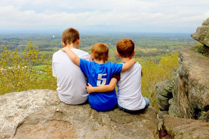 Rear view of three friends sitting on top of cliff
