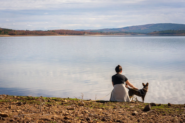 Rear view of woman with dog by lake against sky