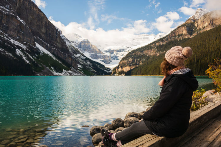 Woman sitting on wood by lake against sky