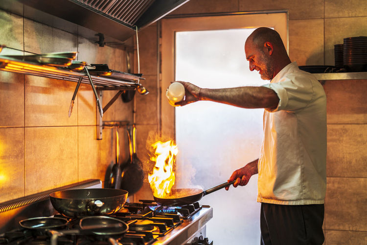 Male chef with burning flame pouring oil in pan