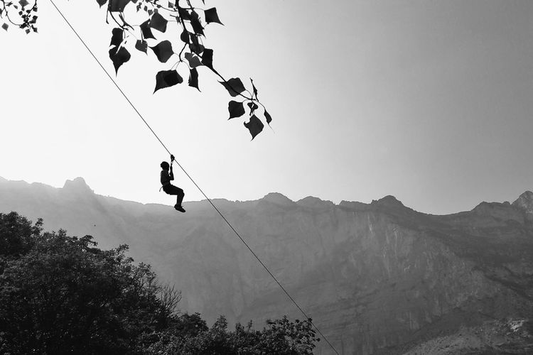 Low angle view of person rappelling on rope against mountains