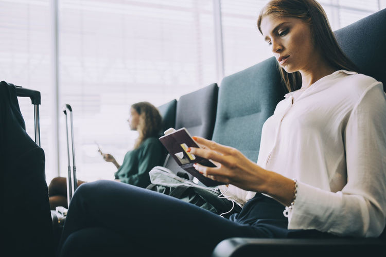 Young businesswoman looking at passport while sitting in airport departure area
